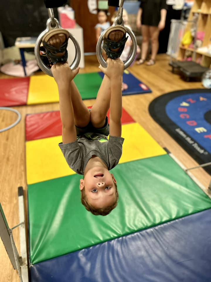 a boy hanging on a monkey ring in tumbling class
